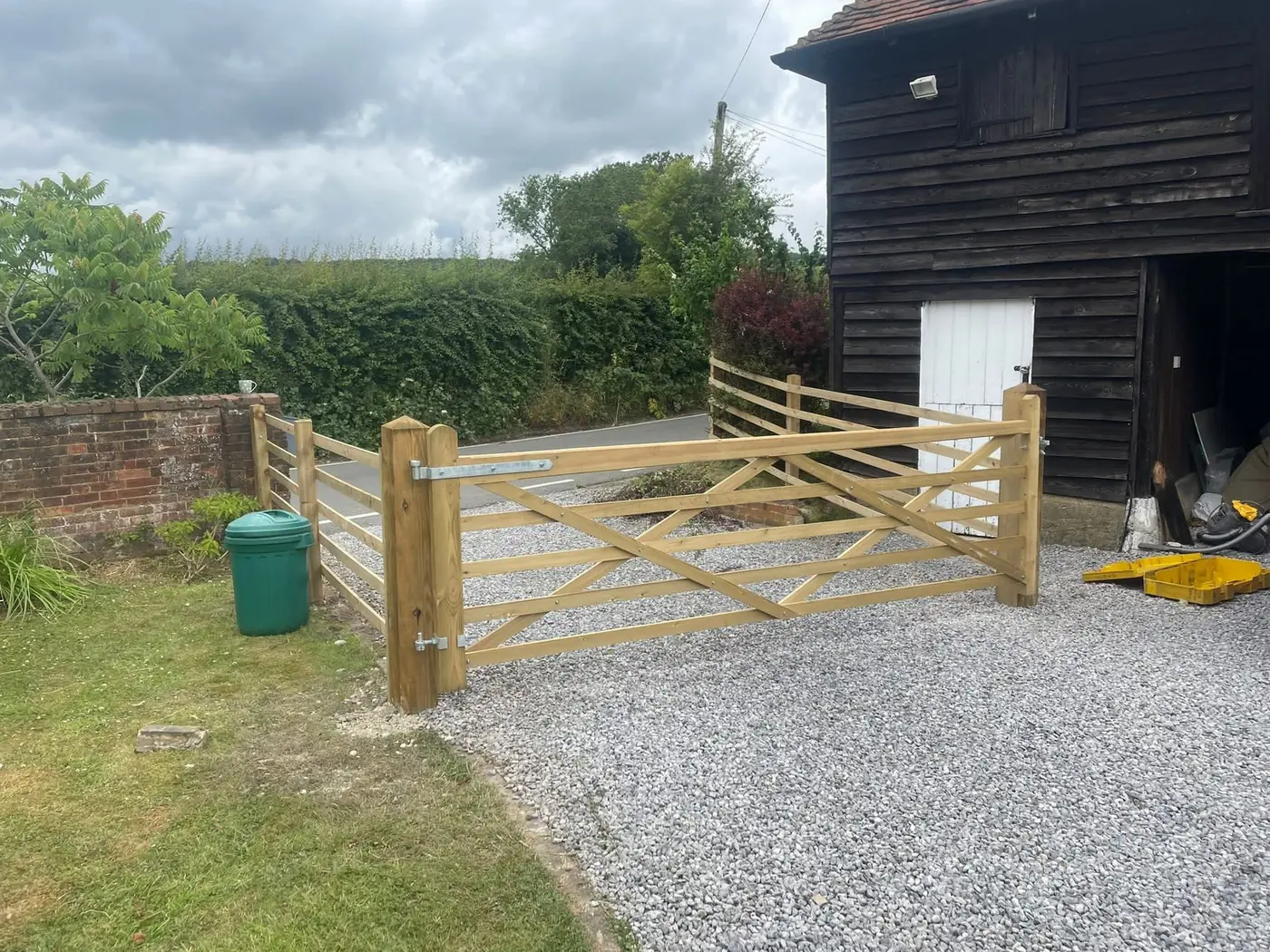 New timber five bar driveway gate on a gravel drive beside a weatherboarded barn, fitted by Tyrrells